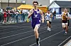 Runner in purple uniform leads a race on a track.