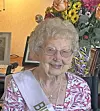 Elderly woman in a floral top smiles at her birthday celebration.