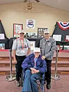 Three veterans at a commemorative event with displays in the background.