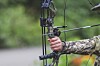 Archer holding a compound bow in a green outdoor environment.
