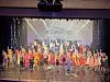 Ensemble cast performing on stage with colorful costumes.