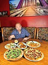 Man at a table with multiple food dishes, including pizzas and appetizers.