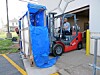 Forklift unloading blue-wrapped cargo at a warehouse entrance.
