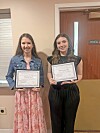 Two students holding certificates in a room.