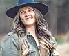 Woman smiling in a forest wearing a hat.