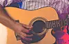 Guitarist's hand playing an acoustic guitar.