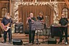 Band performing on stage with instruments and lights in a rustic setting.