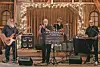 Band performing on stage with instruments and lights in a rustic setting.