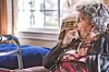 Elderly woman sitting in a chair, looking out the window.