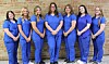 Six healthcare workers in blue scrubs standing together.
