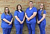 Four individuals in blue scrubs standing in front of a brick wall.