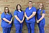 Four individuals in blue scrubs standing in front of a brick wall.