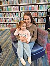 A mother holds her daughter in a library.