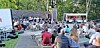 Audience enjoying an outdoor concert with a food truck in view.