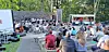 Audience enjoying an outdoor concert with a food truck in view.
