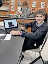 Student smiling at a laptop in a classroom setting.