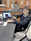 Student smiling at a laptop in a classroom setting.