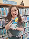 Library staff member with a mug and toys in front of bookshelves.