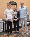Student holding a certificate with two adults in formal attire.