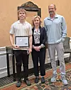 Student holding a certificate with two adults in formal attire.