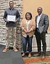 Three people standing together with an award certificate.