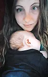 A mother with long hair holds a sleeping baby close to her chest.