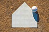 A baseball resting on the edge of a white home plate on a brown dirt field.