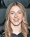 Smiling woman with wavy blonde hair posed indoors against a dark background.