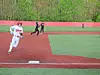 Baseball player in white runs on the infield as two fielders in black watch nearby.