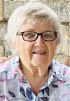 Older woman with white hair and glasses posed in front of a stone wall.