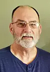 Close-up portrait of a man with glasses and a beard wearing a blue shirt.