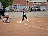 Softball player swings at a pitch while a catcher crouches behind home plate on a dirt field.