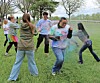 People in casual clothes throw colored powder on a grassy field outdoors.