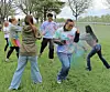 People in casual clothes throw colored powder on a grassy field outdoors.
