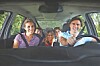 Four people smiling inside a car, viewed from the front seat.