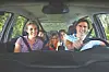 Four people smiling inside a car, viewed from the front seat.