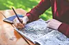 Hands drawing intricate designs in a sketchbook on a wooden table outdoors.