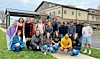 A group of people posing outdoors on grass in front of a large building.