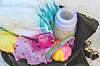 Close-up of a baby bottle, pacifier, bib and clothing items on a bag.