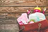 A woven bag holding diapers, a baby bottle, and pacifiers on a rustic wooden surface.