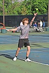 A tennis player tosses the ball and raises a racket on an outdoor court.