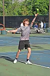 A tennis player tosses the ball and raises a racket on an outdoor court.