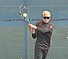 Tennis player holding a racket and preparing to swing on an outdoor court.