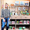 Woman standing next to shelves displaying framed artwork and colorful prints.