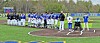Two youth baseball teams stand in a line on an artificial-turf field before play.