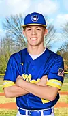 A baseball player in a blue and yellow uniform stands with arms crossed outdoors.