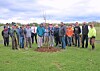 A group of people standing in a field beside a newly planted tree.