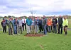 A group of people standing in a field beside a newly planted tree.