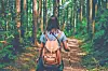 Person with a backpack walking on a forest trail surrounded by tall trees.