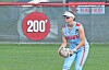 Softball player in light blue uniform crouches in the outfield holding a glove near a red 200-foot marker.